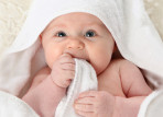 Close up portrait of a cute baby wrapped in a white towel chewing on the towel